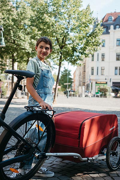 Happy girl with Croozer cargo bike trailer in lava red - urban cycling and sustainable city transport
