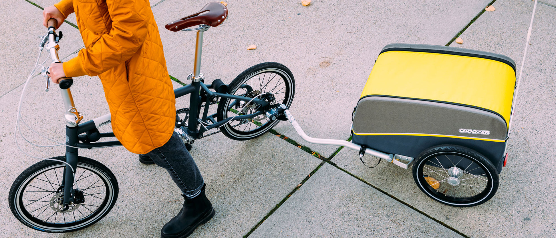 Woman stands astride folding bike with Croozer Cargo trailer attached, ready to ride.
