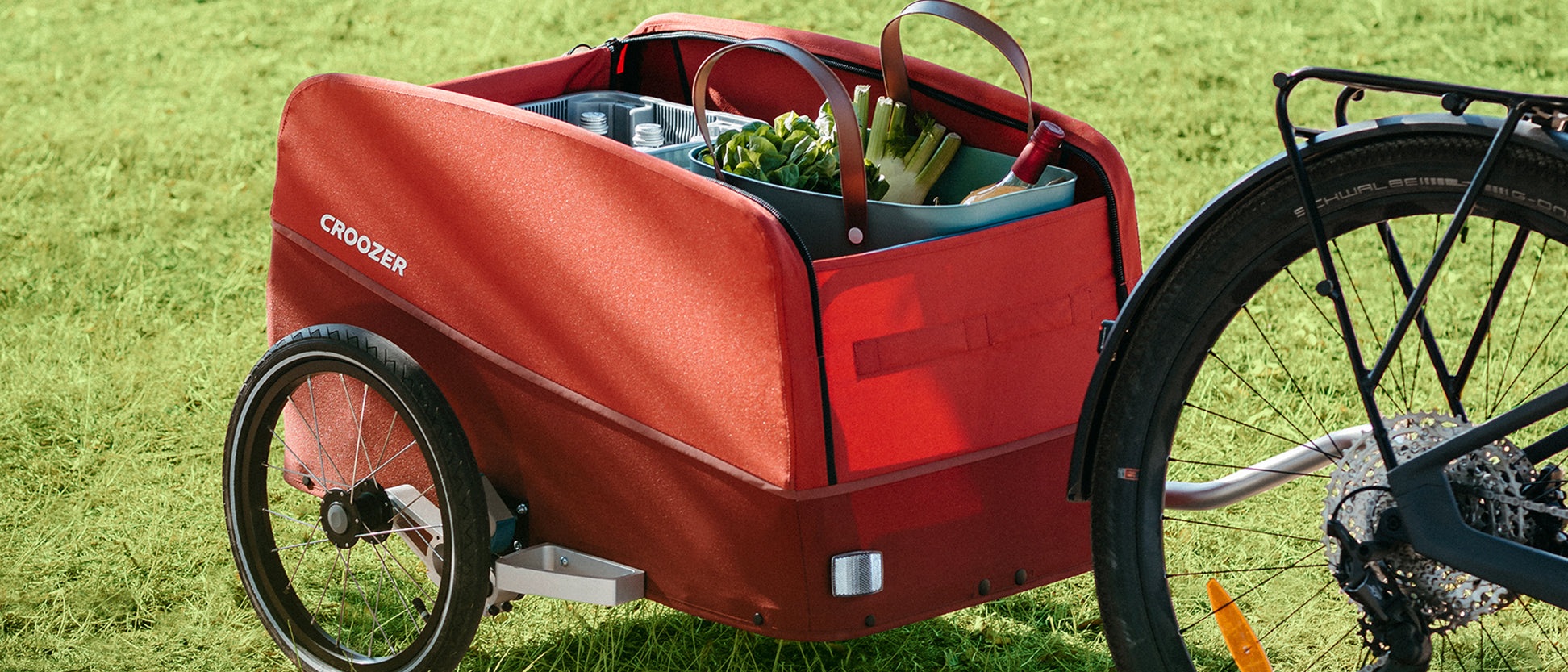 Croozer Cargo trailer on a meadow, hitched to a bike and loaded with water, veggies, and wine.