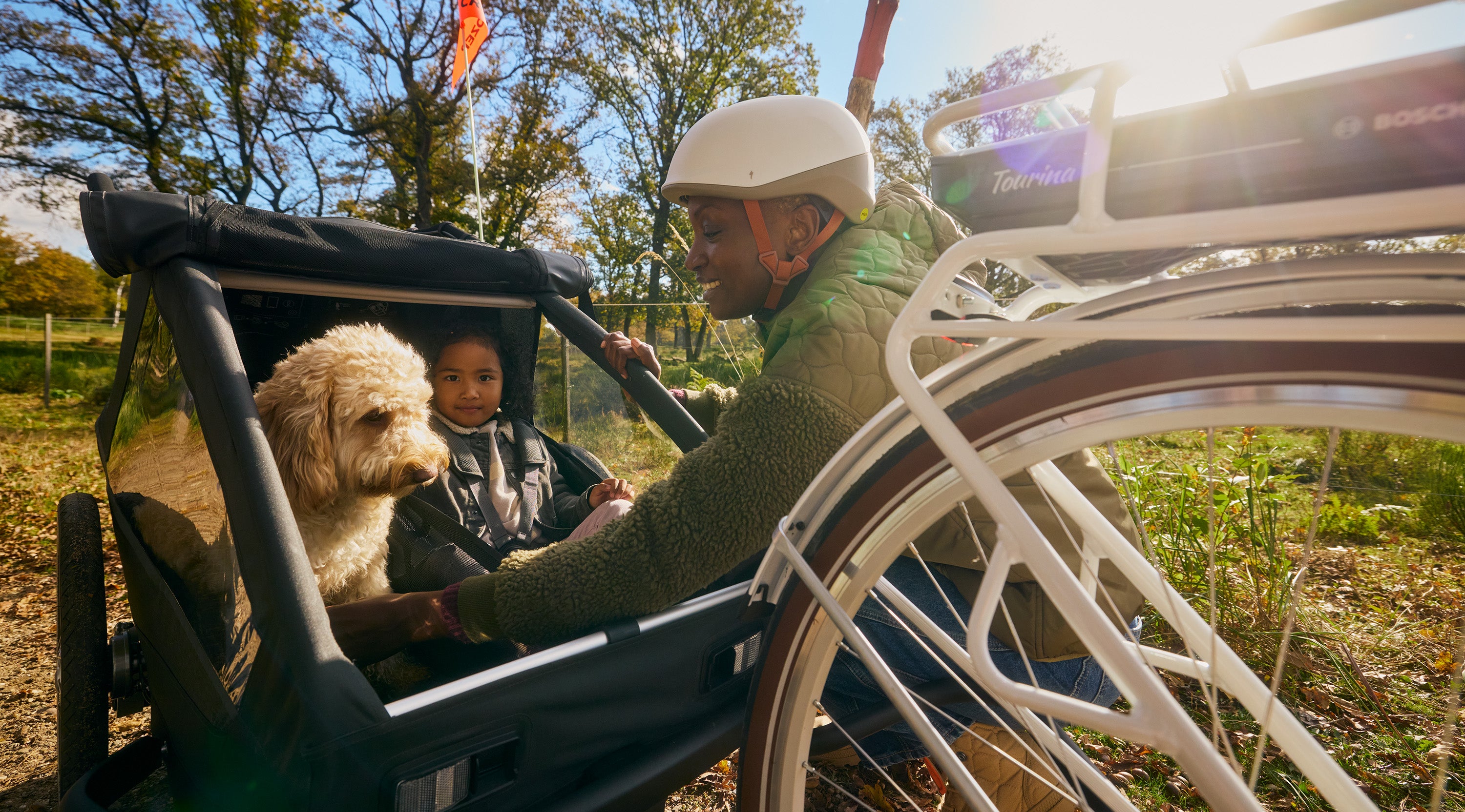 Lächelnde Mutter bei sonnigem Tag unterwegs mit Kind und Hund im Croozer Yuuna