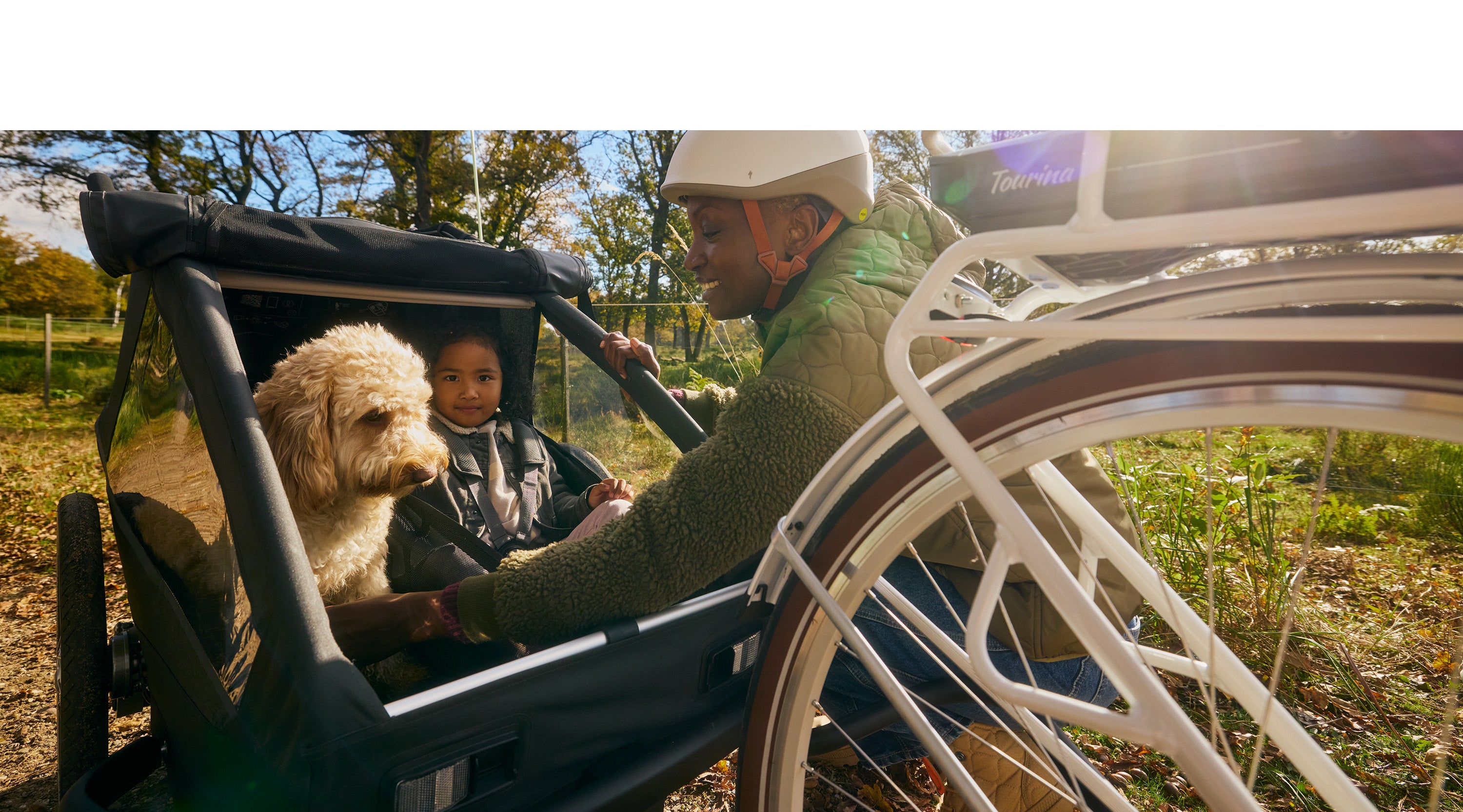 Lächelnde Mutter bei sonnigem Tag unterwegs mit Kind und Hund im Croozer Yuuna