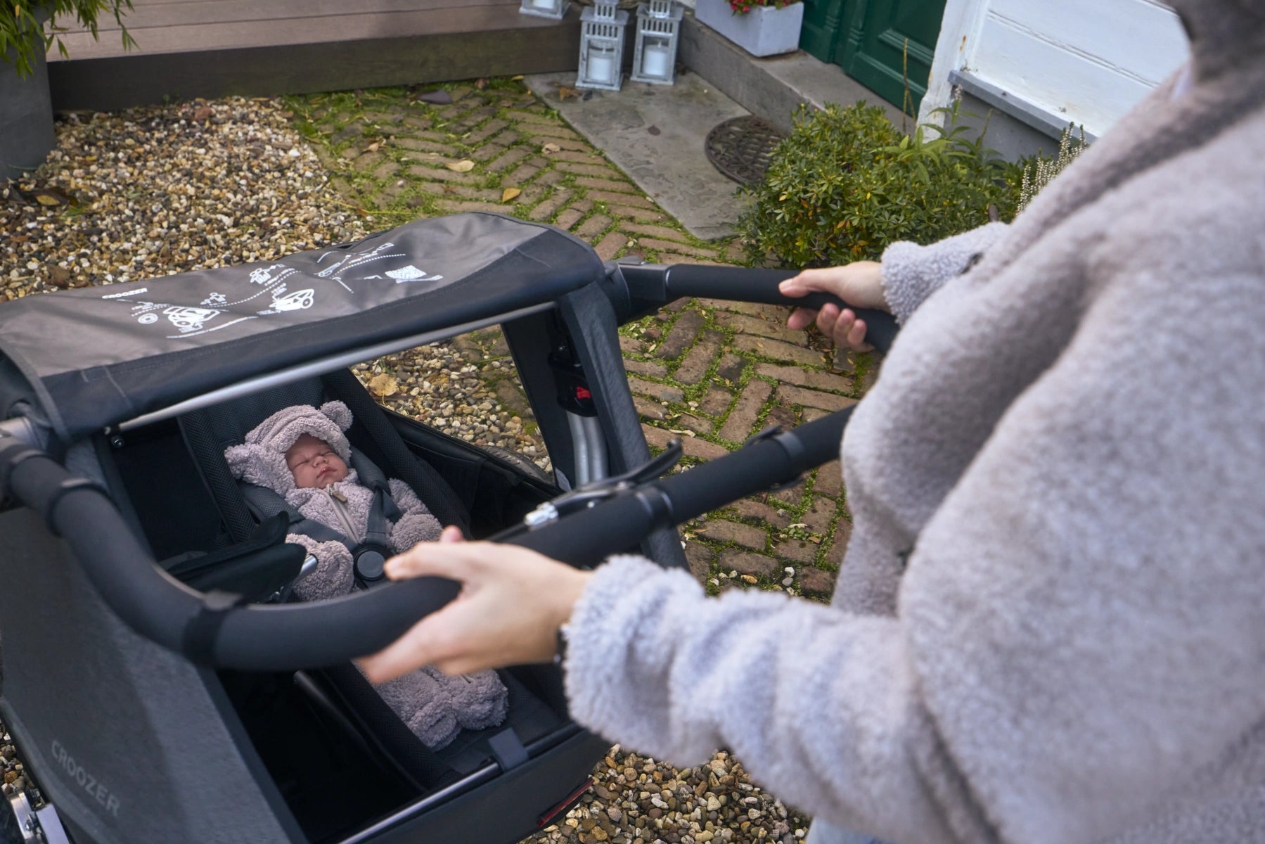 Schlafendes Baby auf der modularen Babyliege, geschützt im Croozer Yuuna, Mutter am Schiebebügel