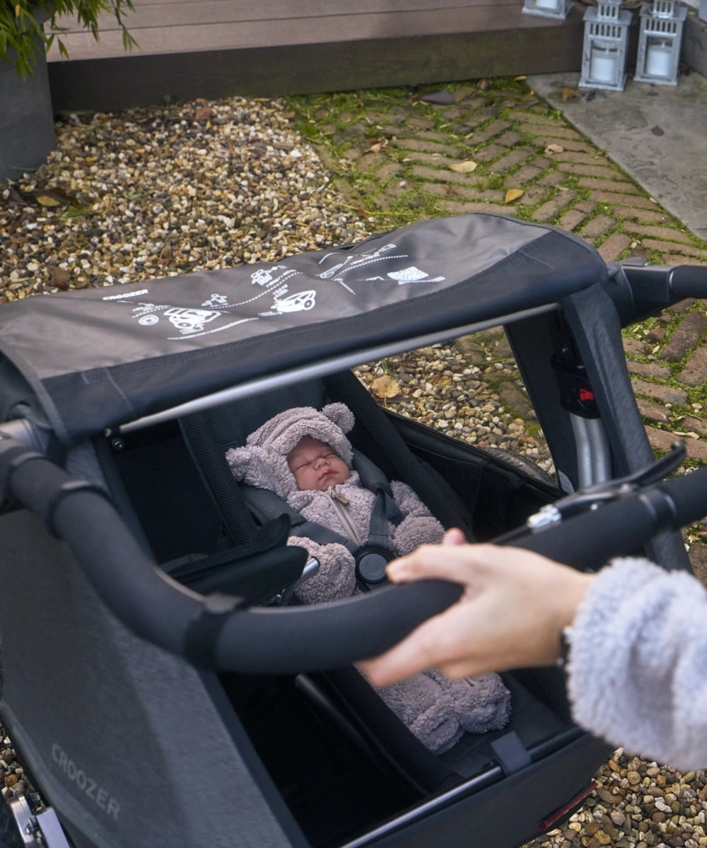 Schlafendes Baby auf der modularen Babyliege, geschützt im Croozer Yuuna, Mutter am Schiebebügel