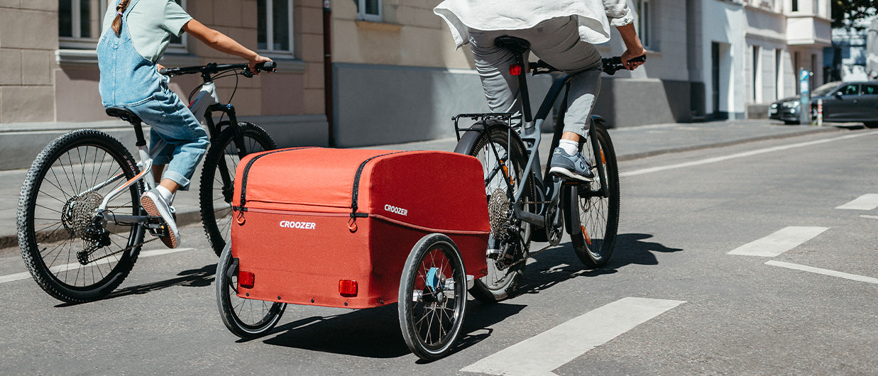 Father and daughter cycling with Croozer cargo bike trailer - urban transportation and city commuting