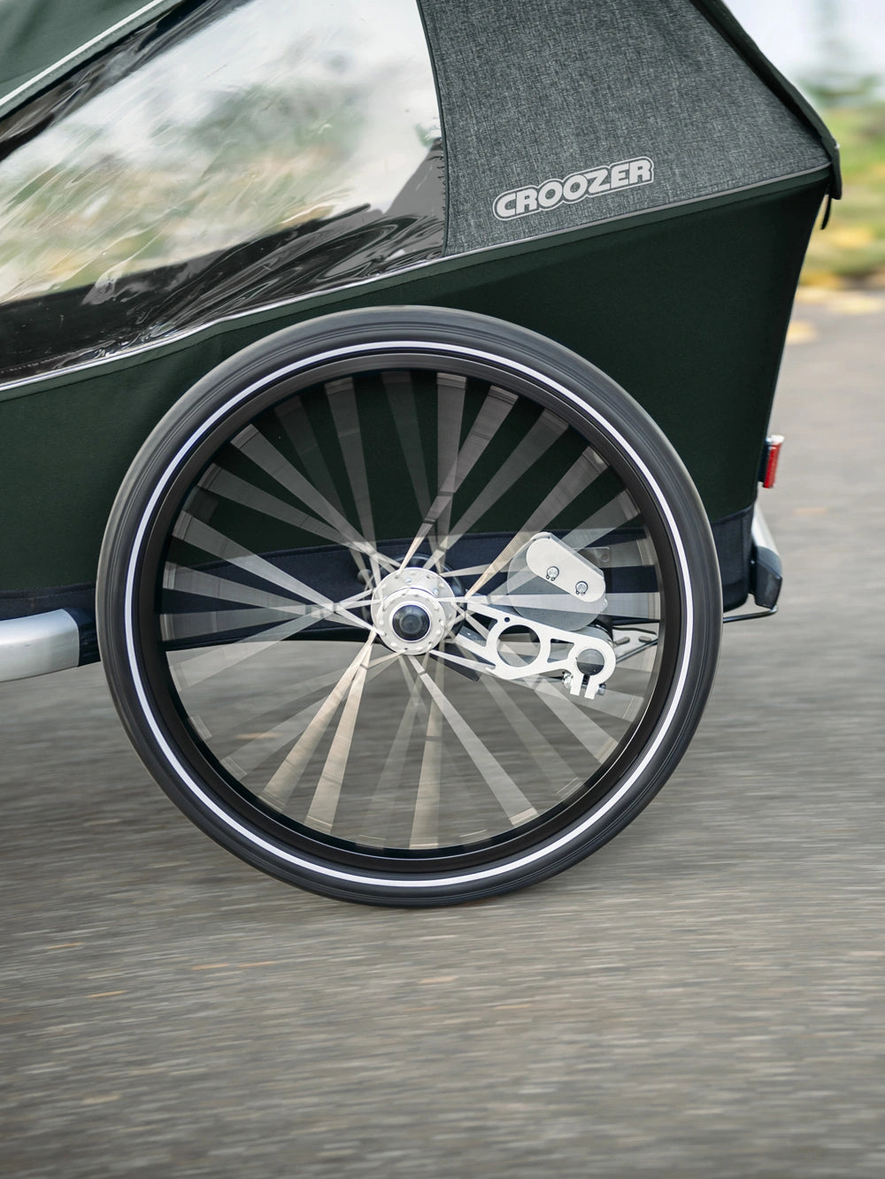 Close-up of wheel on jungle green Croozer Kid Vaaya trailer featuring airpad suspension during ride