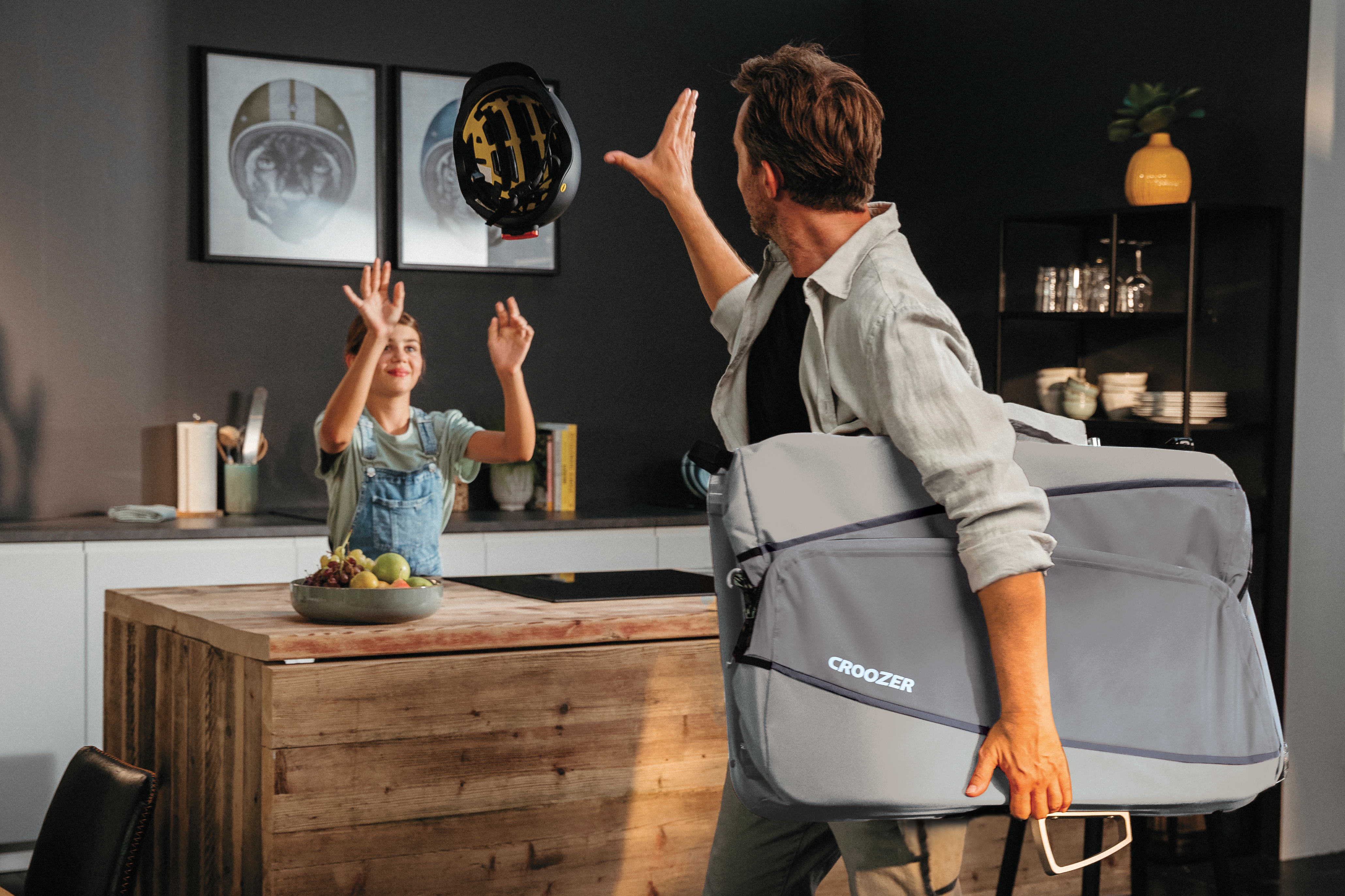 Father and daughter preparing for bike tour with Croozer trailer, passing helmet to daughter