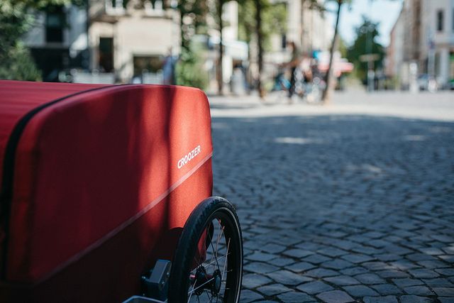 Croozer cargo bike trailer in lava red on cobblestone street - urban cycling and city transport