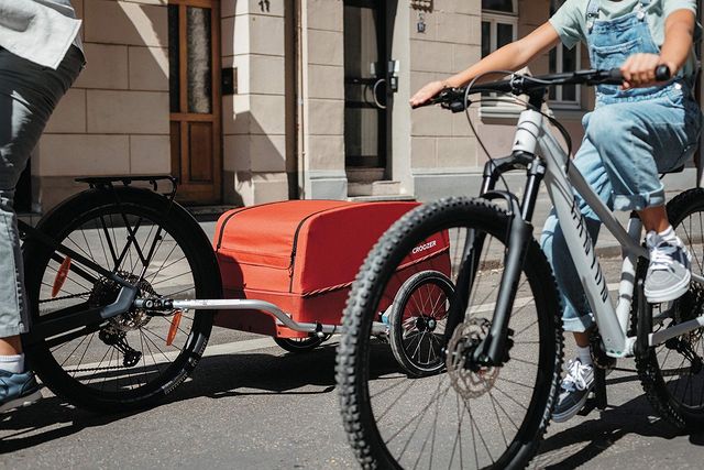 Father and daughter on city bike tour with Croozer cargo bike trailer in lava red