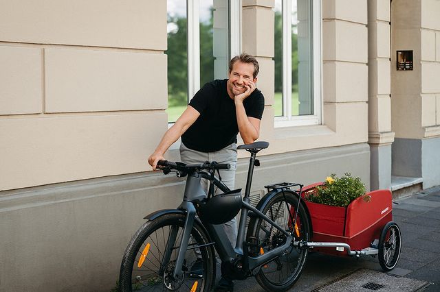 Happy man with e-bike and Croozer cargo trailer - urban cycling and sustainable transport solution