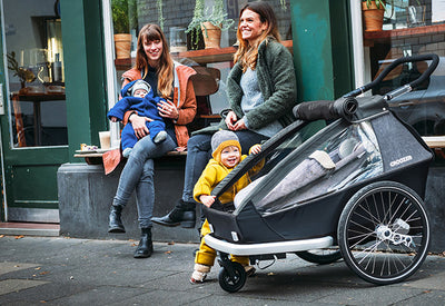 Two smiling women and their children in front of local store - Croozer Kid trailer as buggy with them