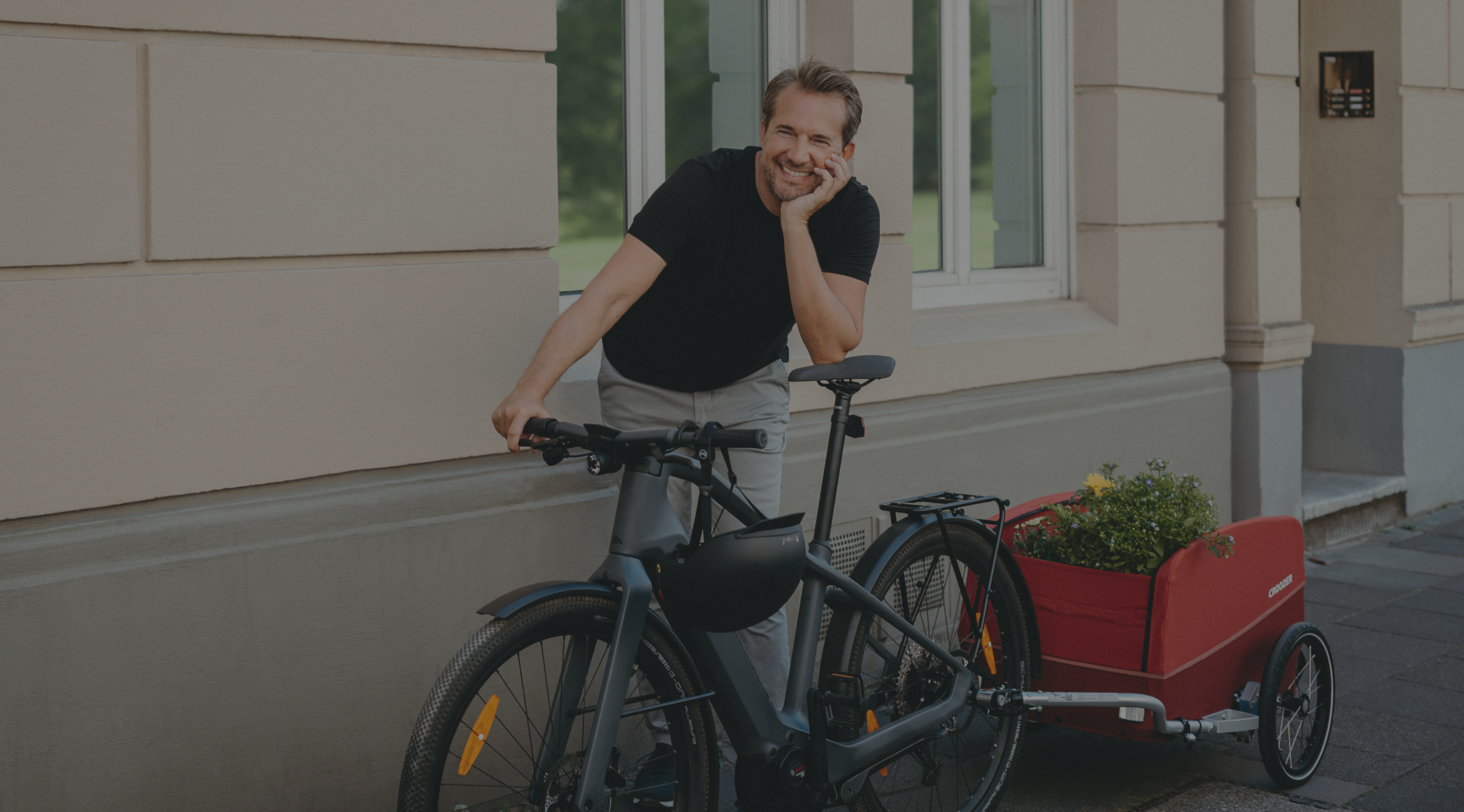 Junger Mann mit Fahrrad und beladenem Croozer Fahrradanhänger auf dem Gehweg wartend