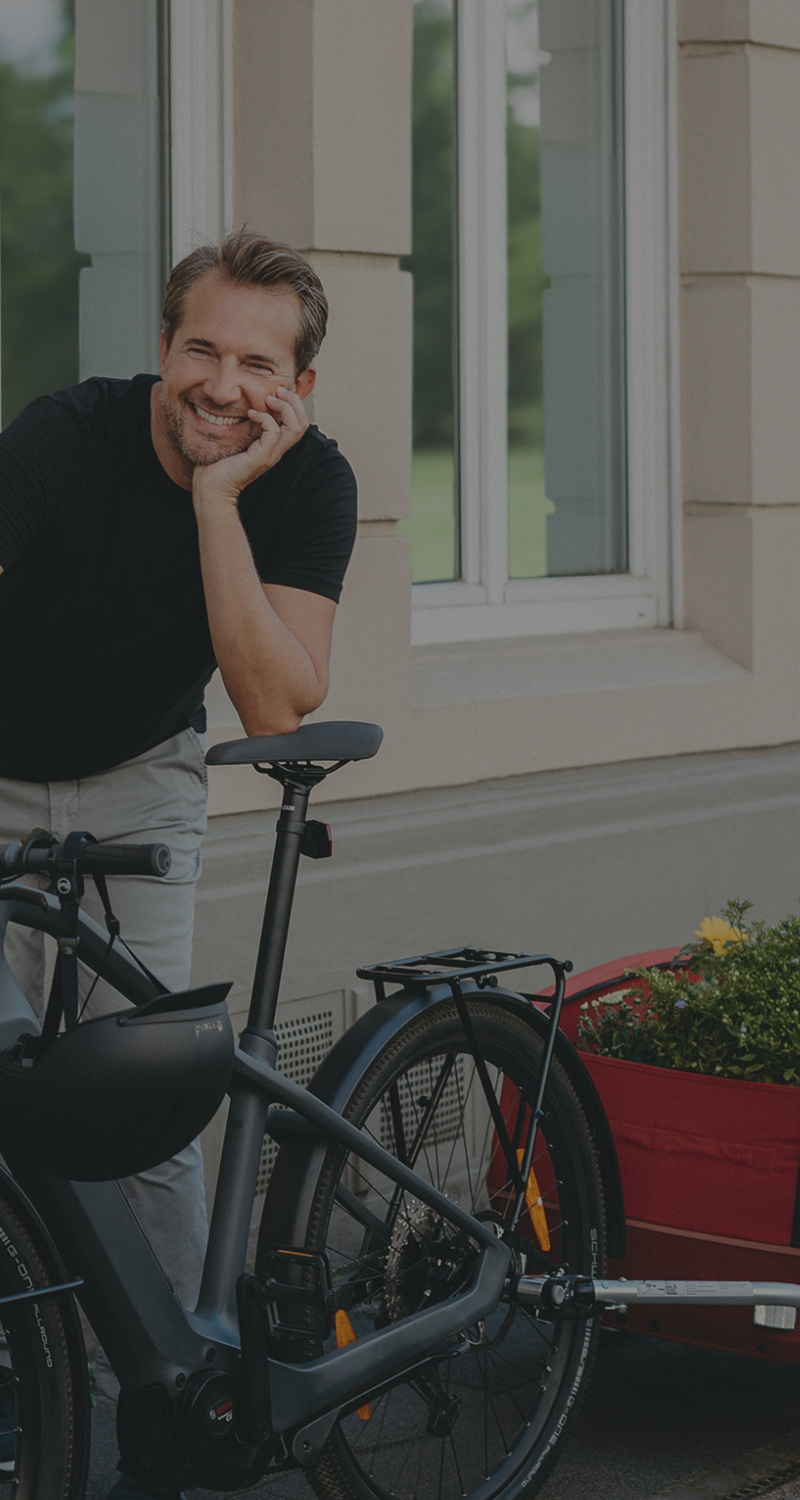 Fahrrad mit rotem Anhänger und jungem Mann stehend