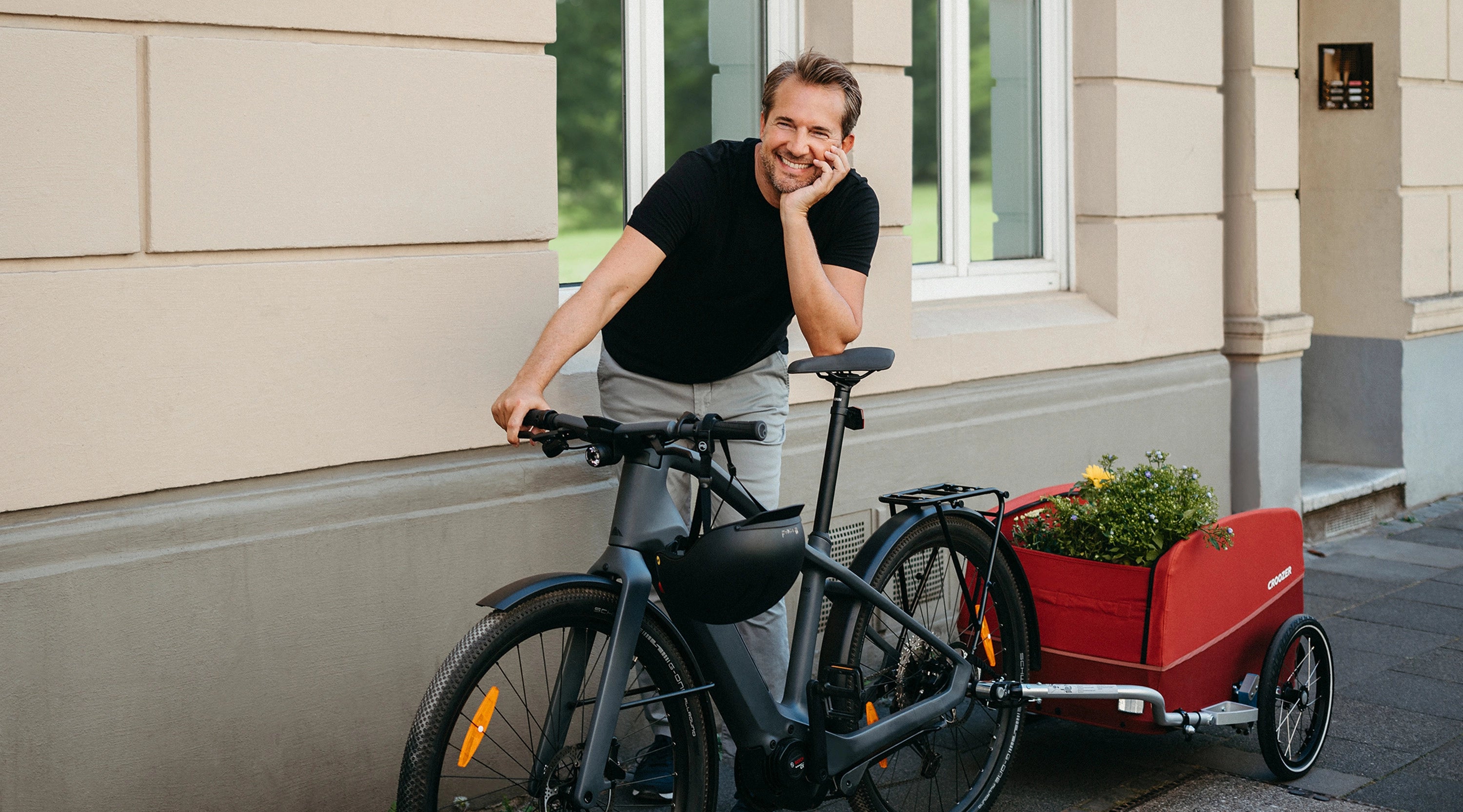 Happy man standing with bike and Croozer Cargo Tuure in front of a house