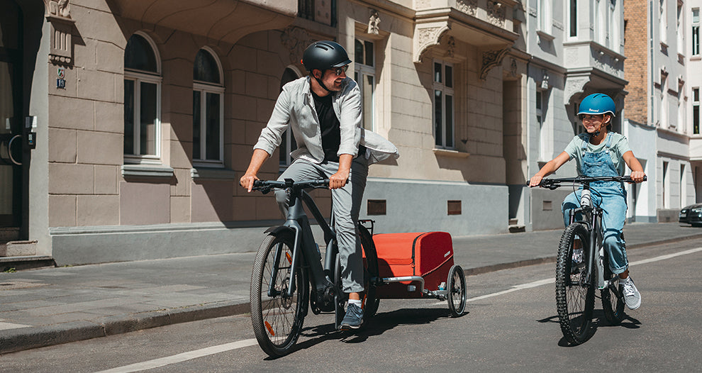 Smiling father and daughter cyling through city with Croozer Cargo bike trailer - front view
