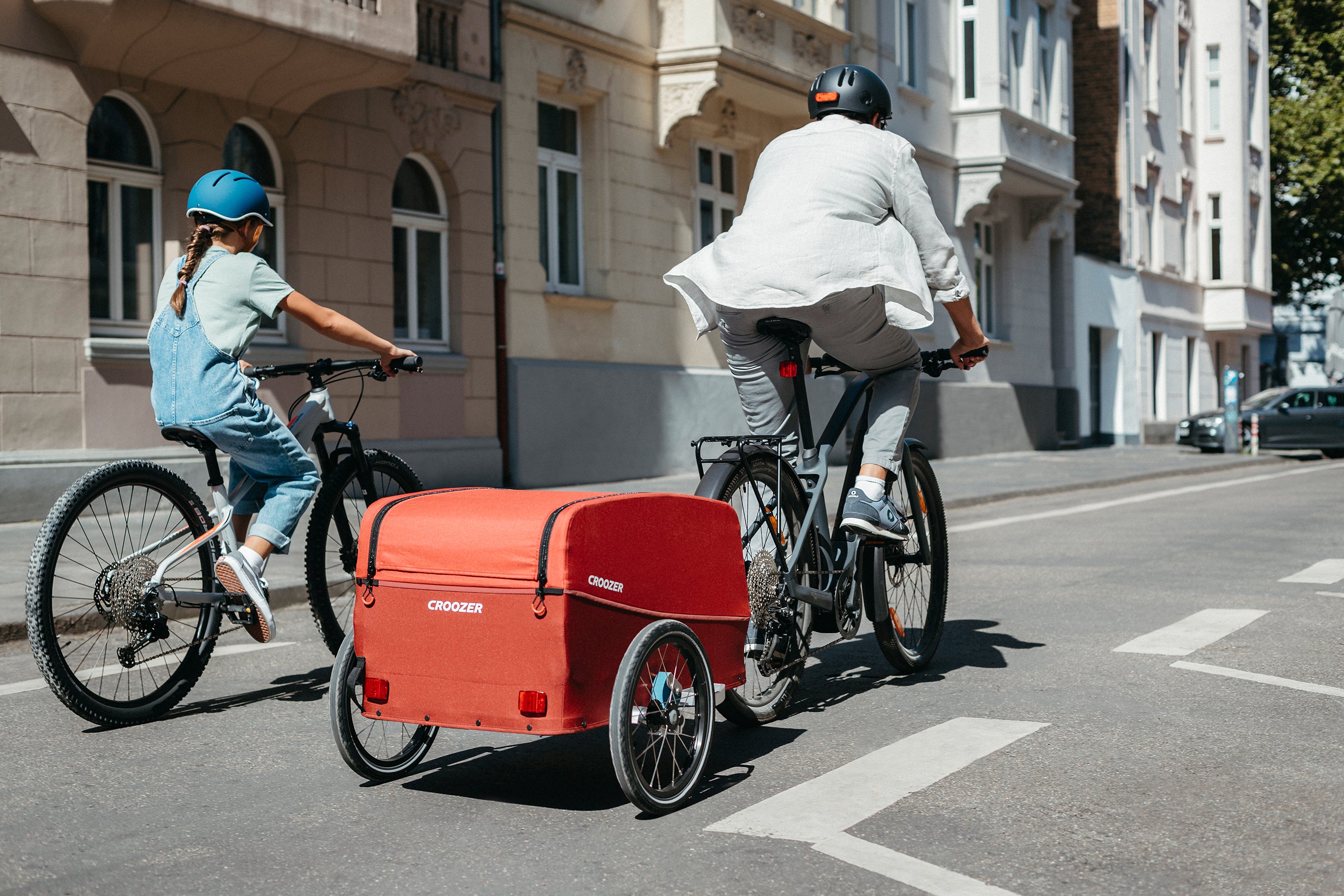 Father and daughter cyling through city with Croozer Cargo bike trailer - back view