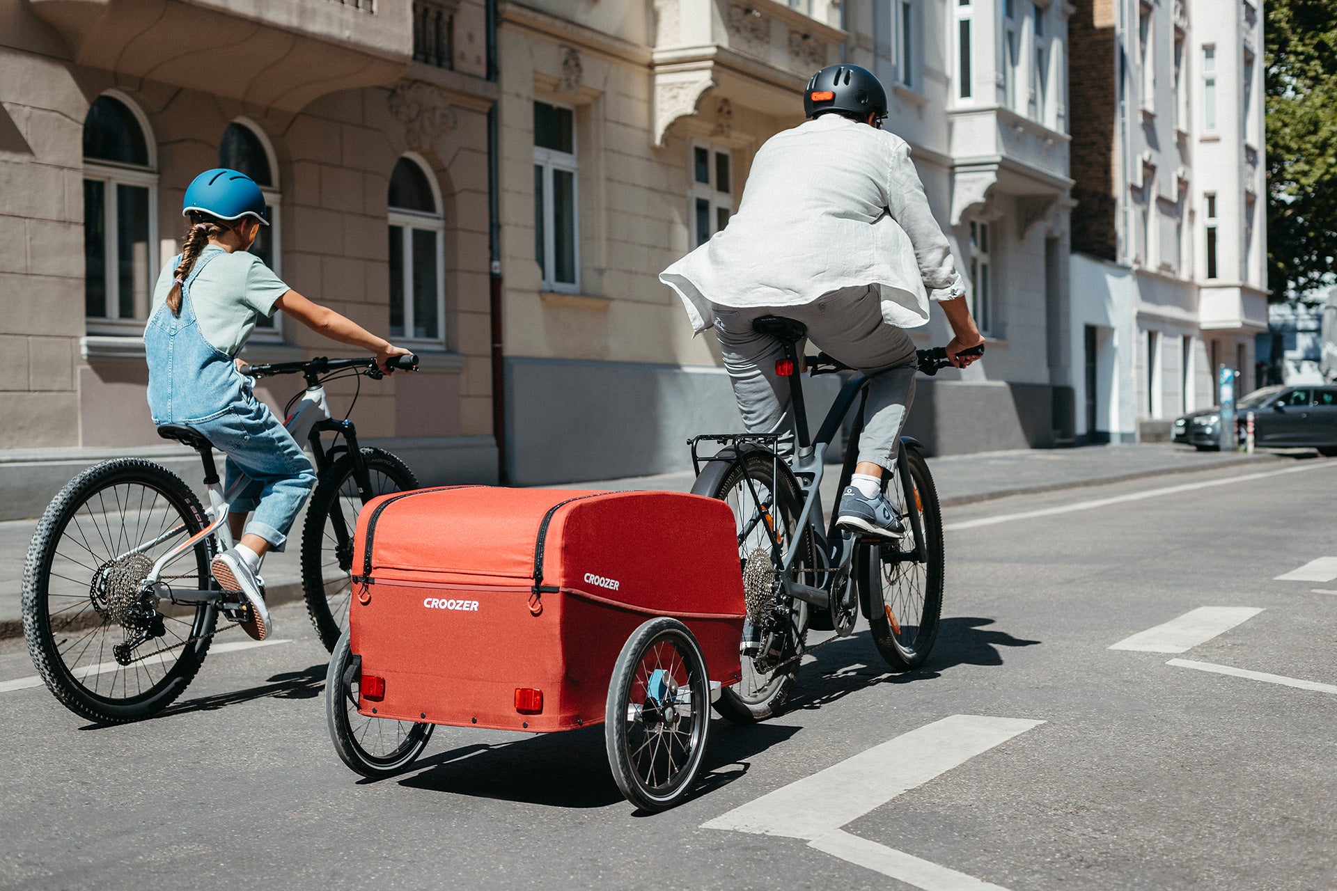 Father and daughter cyling through city with Croozer Cargo bike trailer - back view
