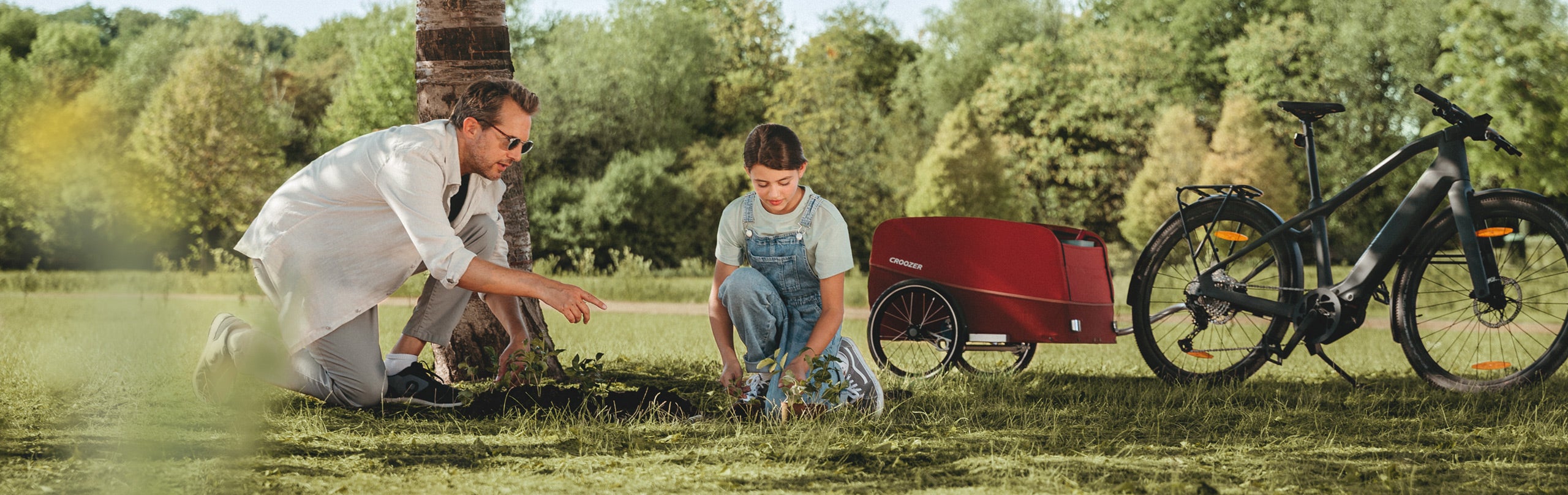 Father and child planting a tree in nature - Croozer Cargo Tuure with them