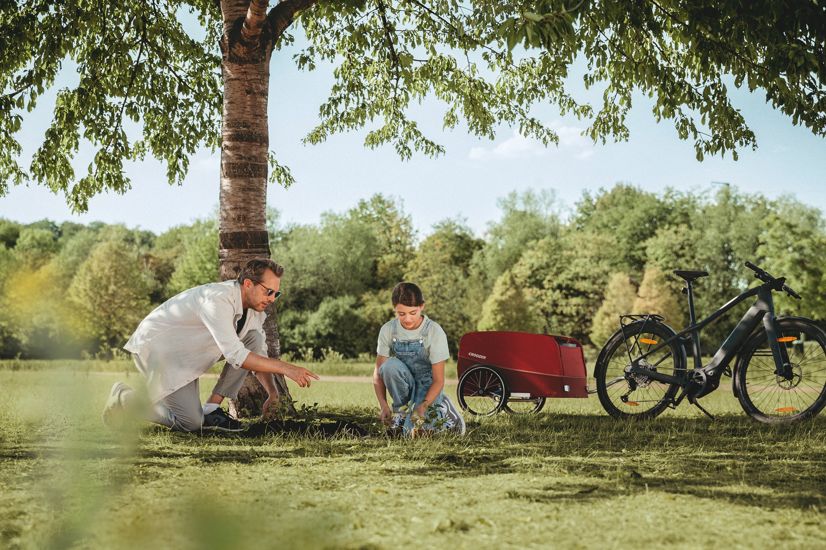 Father and child planting a tree in nature - Croozer Cargo Tuure with them