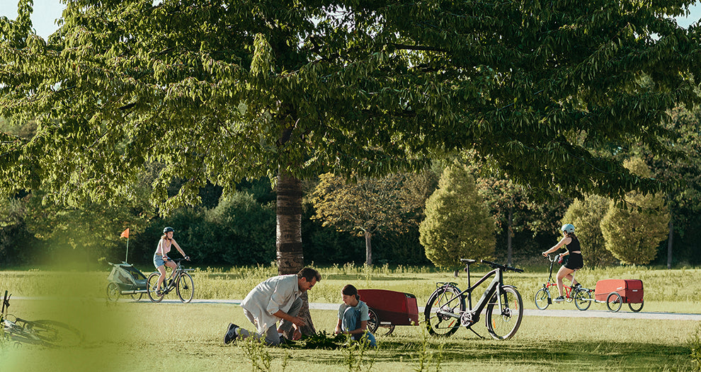 Father and child planting a tree in nature - view from afar, people on the street with Croozer Cargo and Croozer Kid trailers
