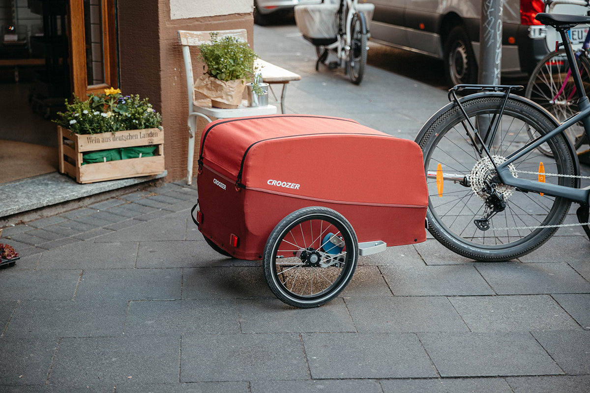 Croozer cargo bike trailer in red parked on city street - urban cycling and local shopping transport