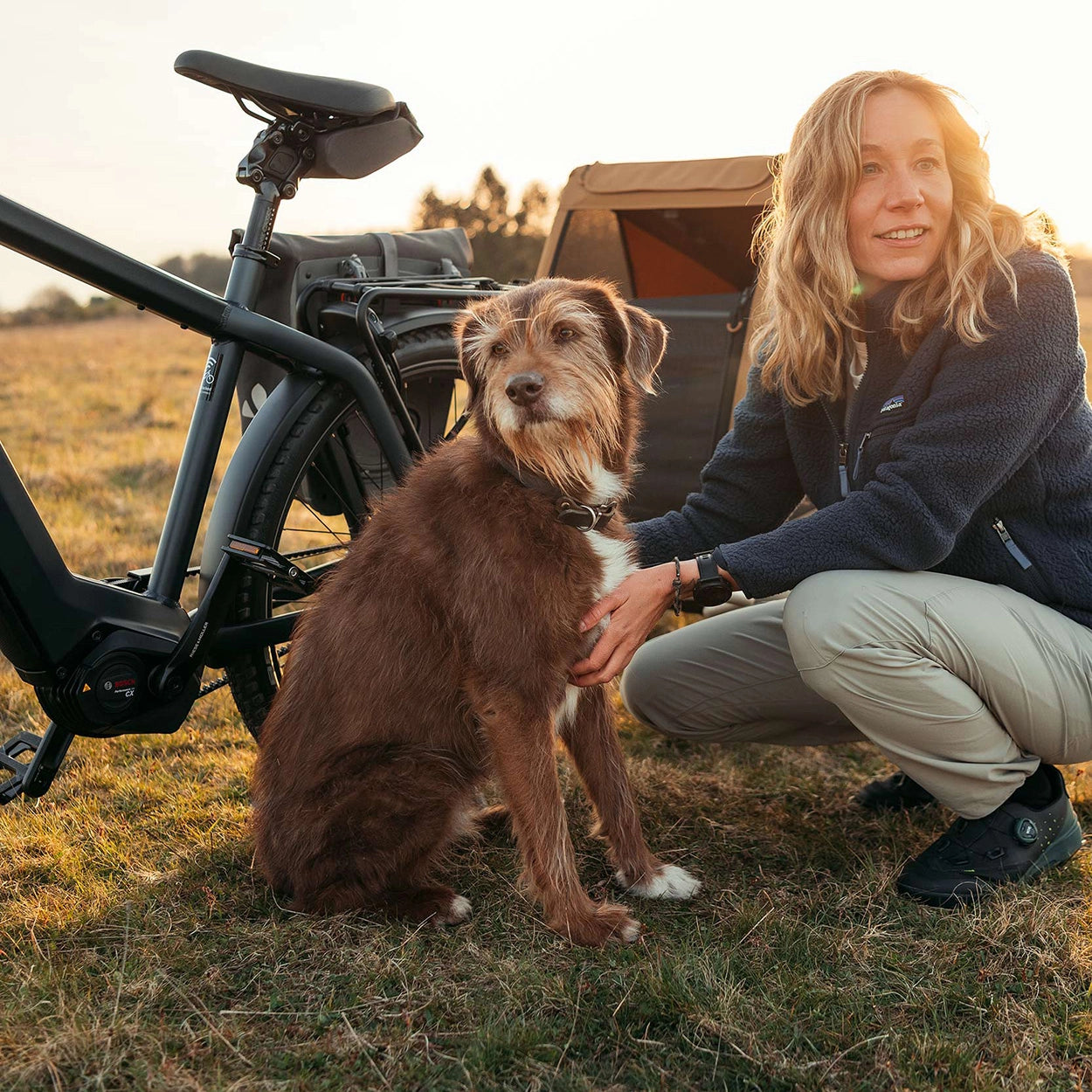 Woman enjoying moment with her dog next to bicycle equipped with Croozer Dog trailer in grassy landscape
