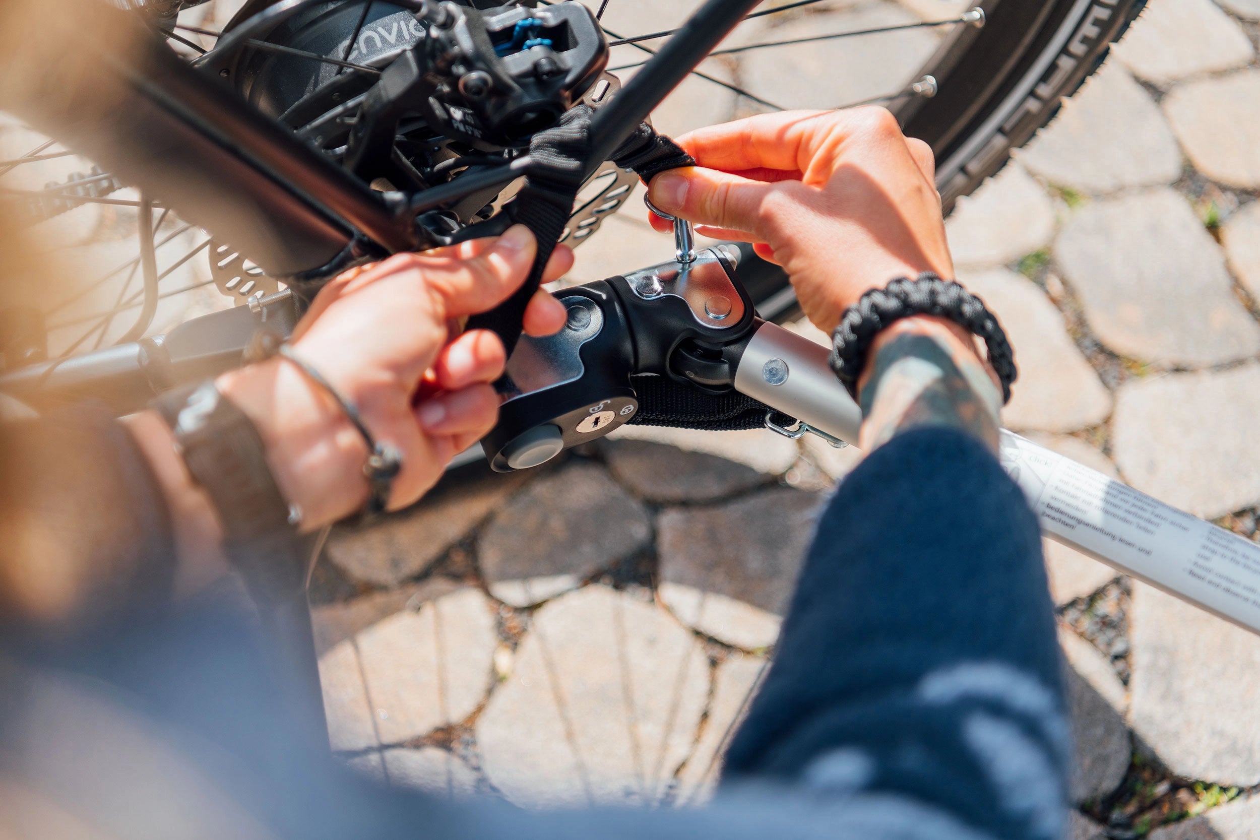 Person fastening safety strap to secure Croozer Dog Outdoor trailer hitch connection