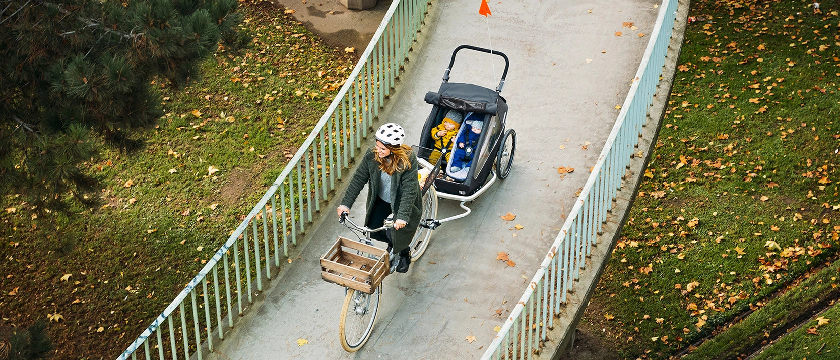 Women cycling across bridge with toddler and baby in Croozer Kid Vaaya trailer during fall season