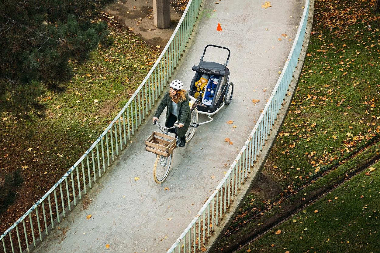 Women cycling across bridge with toddler and baby in Croozer Kid Vaaya trailer during fall season