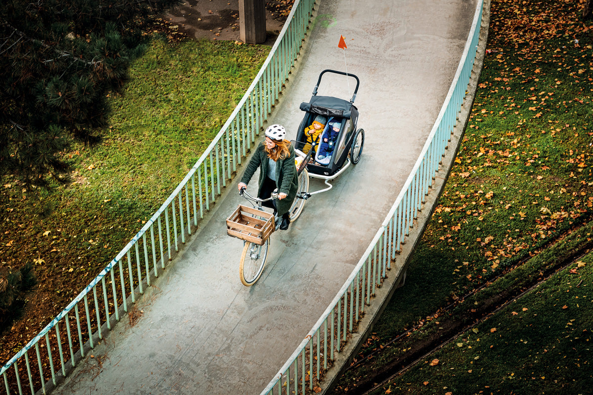 Smiling mother riding with bike over bridge - Croozer Kid bike trailer and her two kids with her