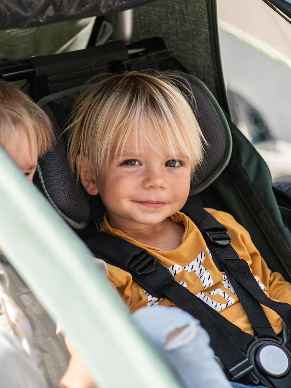 Boy sitting next to his brother in Croozer Kid Vaaya two-passenger bike trailer, smiling at camera