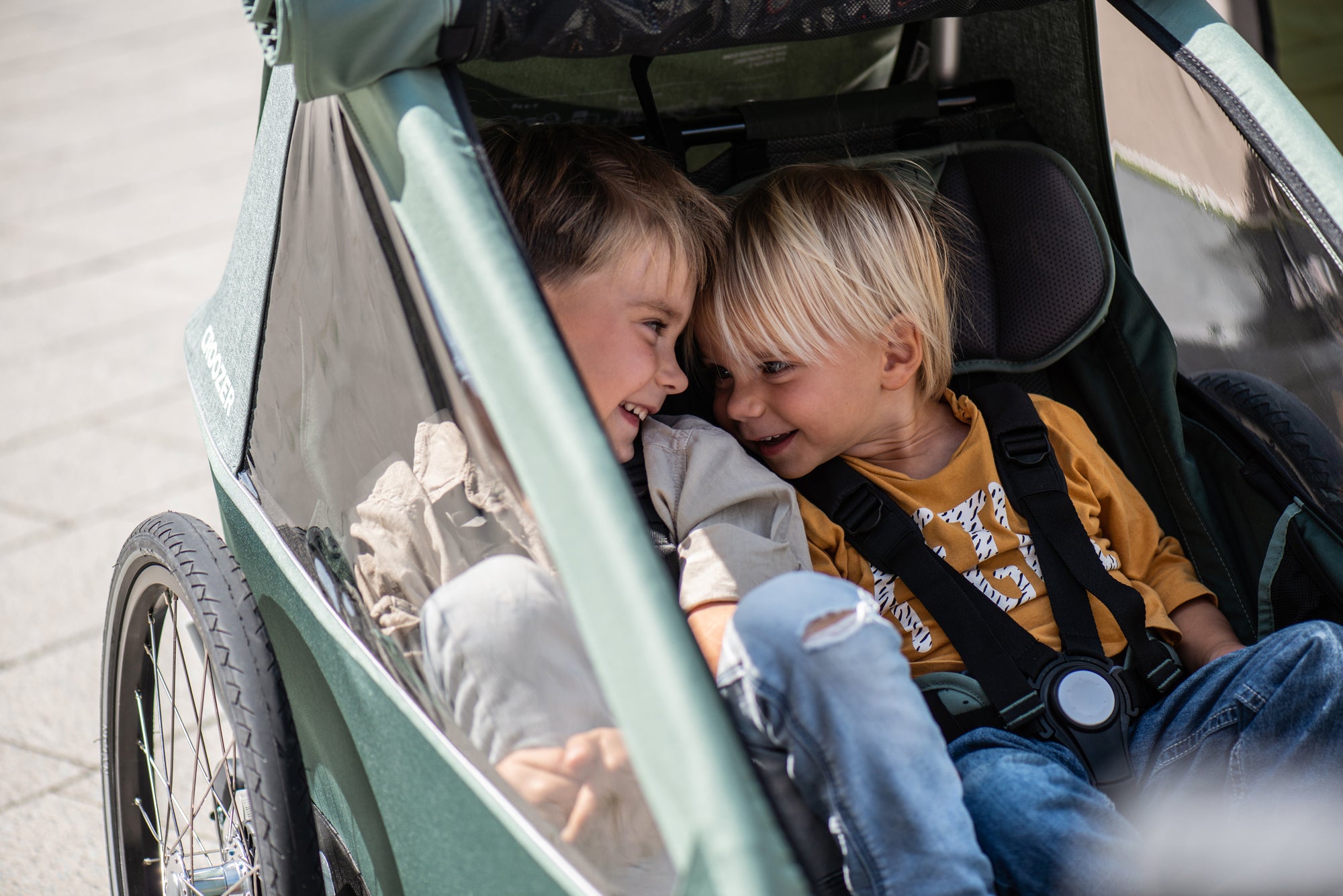 Two happy siblings sitting next to each other in Croozer Kid bike trailer