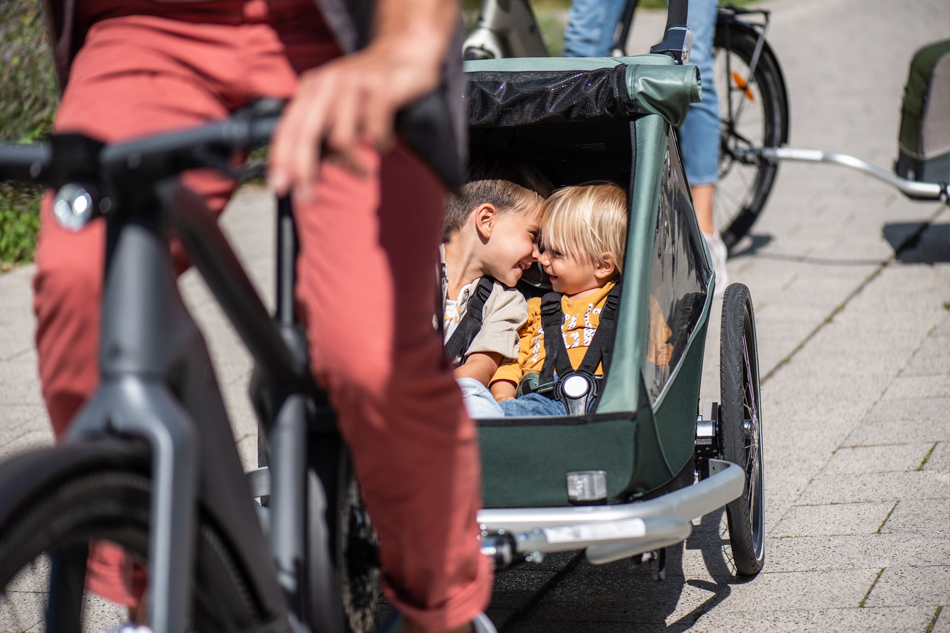 Two happy siblings sitting next to each other in Croozer Kid bike trailer - parent is riding bike
