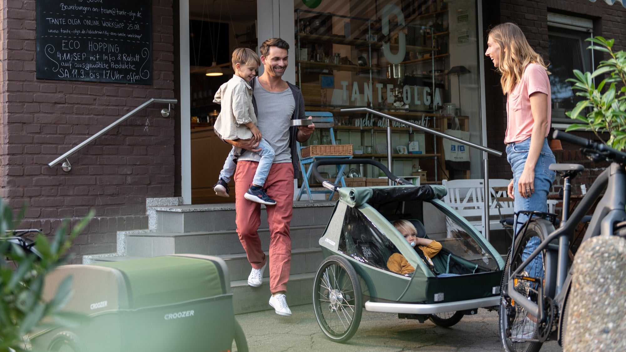 Happy family in the city together with Croozer Kid bike trailer two-seater and their two kids