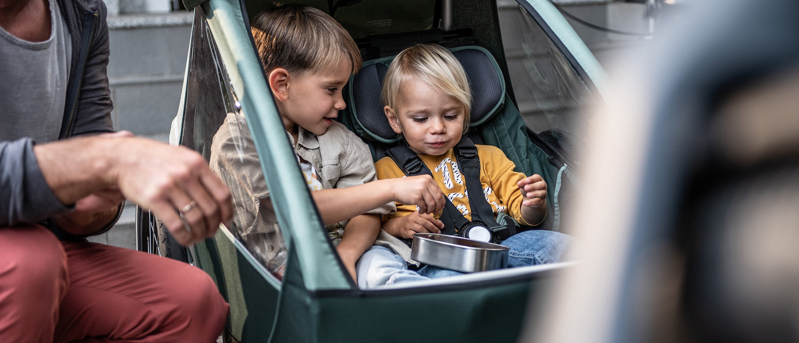 Two siblings sitting next to each other enjoying snacks in Croozer Kid bike trailer