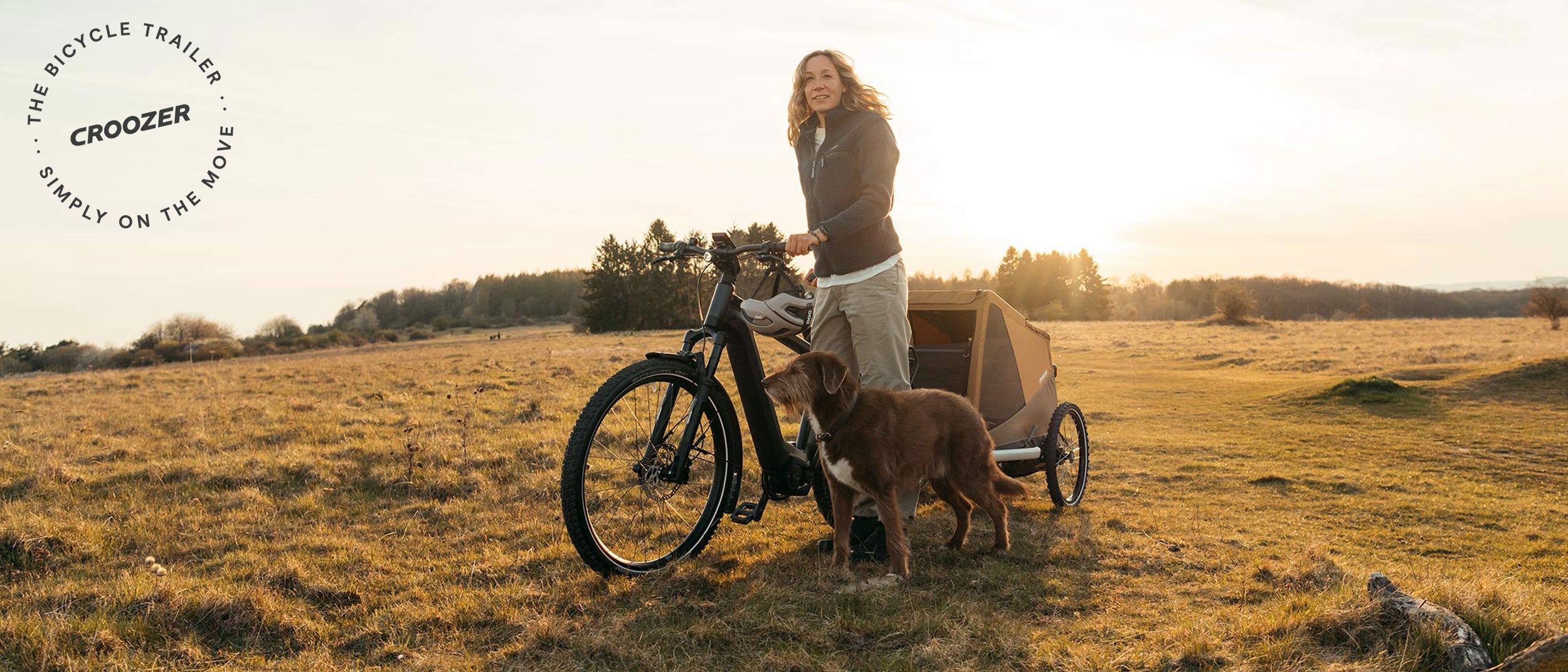 Woman and dog taking a break from bike tour at sunset, Croozer Dog trailer with them - Simply on the move