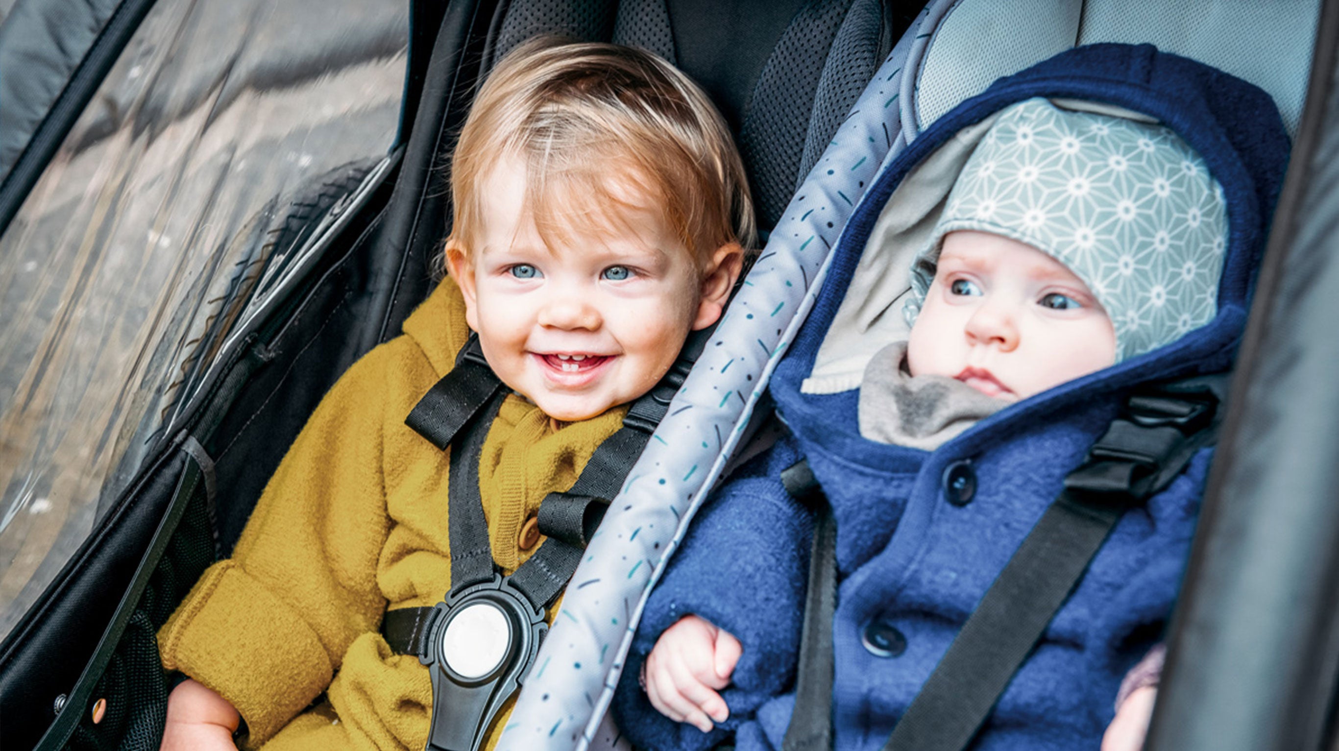 Two happy children sitting next to each other in Croozer Kid bike trailer - 5-point belt system in use