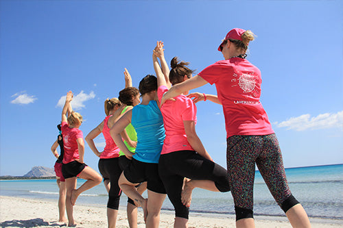 Group of women doing beach fitness workout with arms raised on tropical white sand beach with blue ocean
