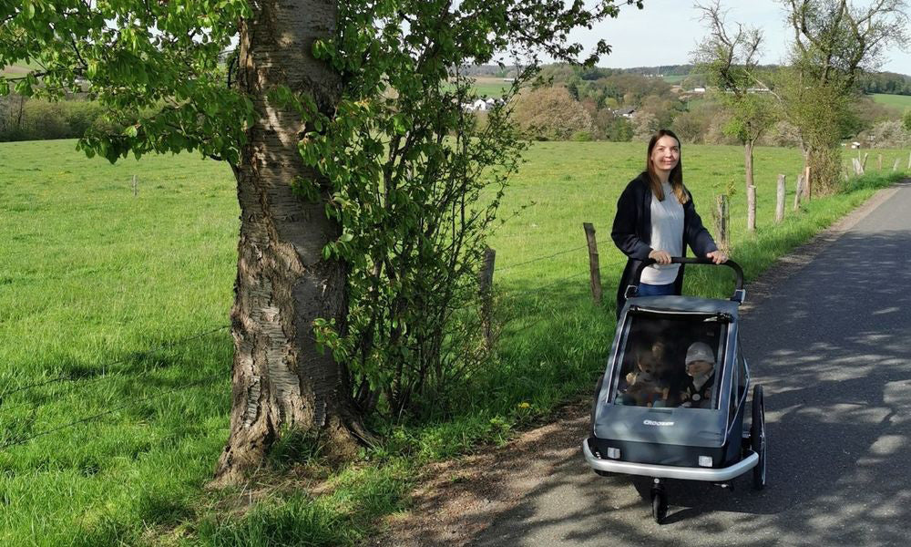 Mother pushing Croozer Vaaya in graphite blue in stroller mode with two children on rural country road