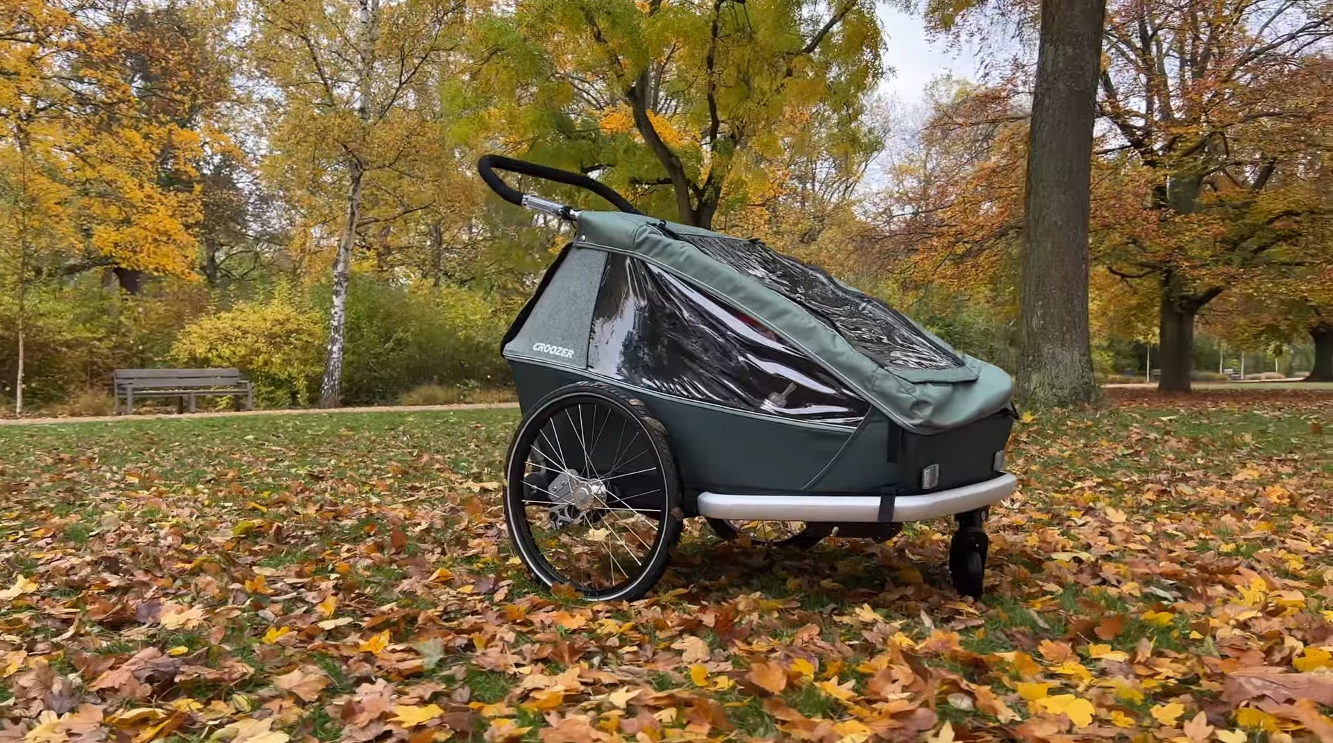 Croozer Kid Vaaya bike trailer in jungle green parked on autumn leaves in park with colorful fall trees