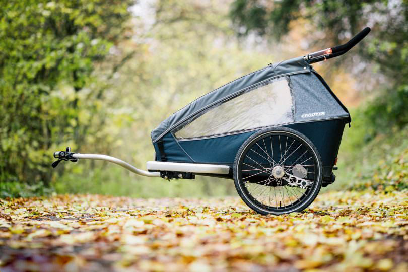Croozer Kid Vaaya bike trailer in graphite blue on autumn path with fallen leaves and trees
