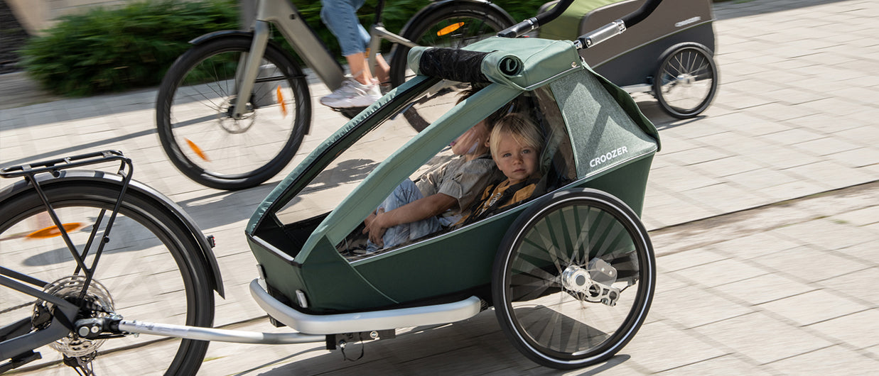Croozer child bike trailer in green carrying young passenger during city ride