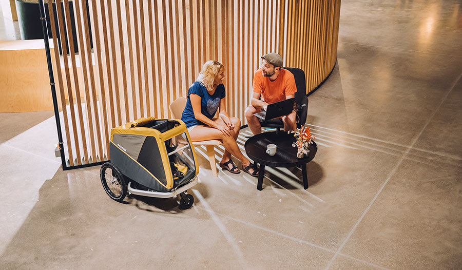 Croozer co workers sitting beside yellow Croozer dog trailer in modern office setting