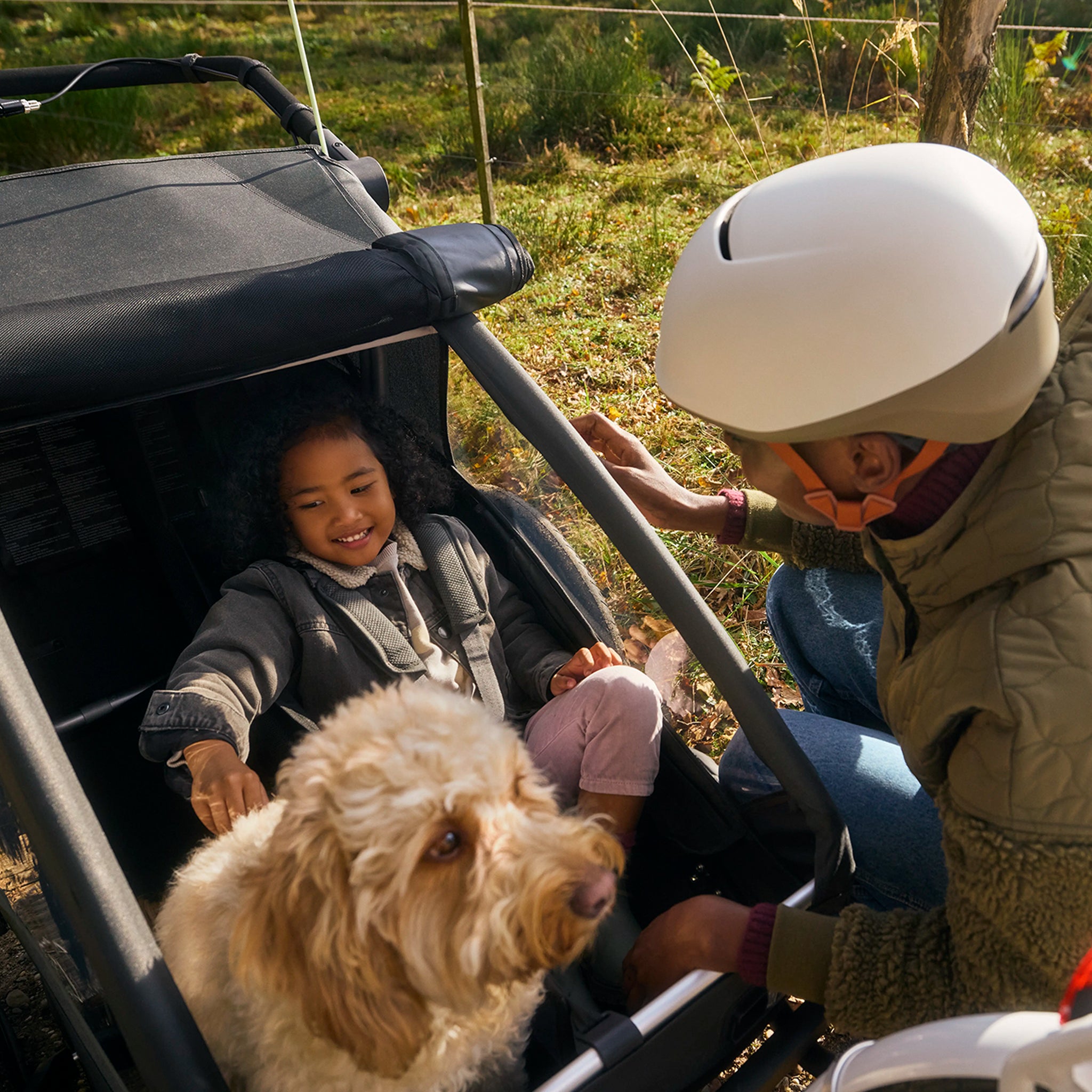 Zu dem Fahrradanhänger Yunna mit Kind und Hund kniet sich eine Frau. 