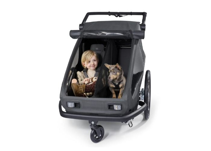 Young child in premium seat and small dog in dog module sharing Croozer Yuuna modular trailer