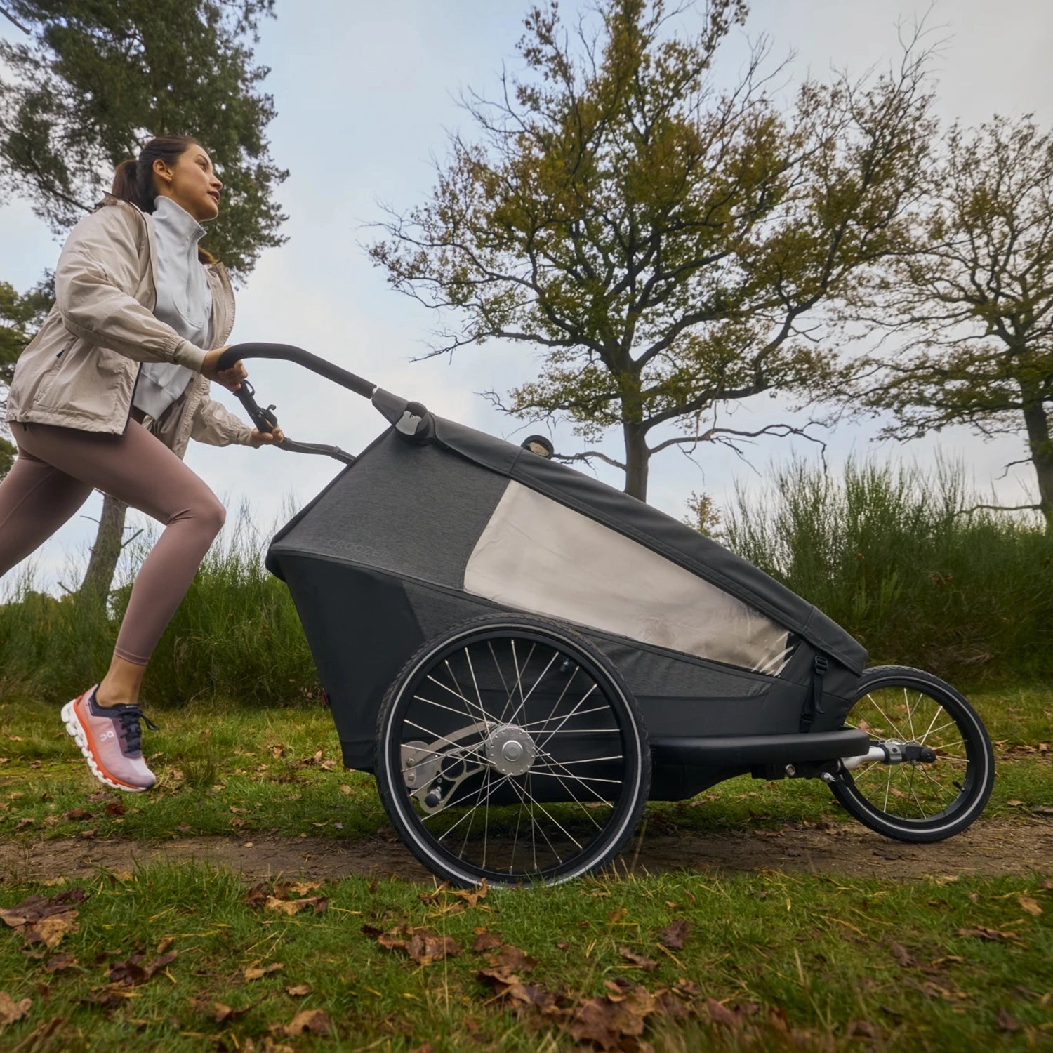 Mother jogging with Croozer Yuuna trailer in jogger mode along natural trail, lifestyle scene