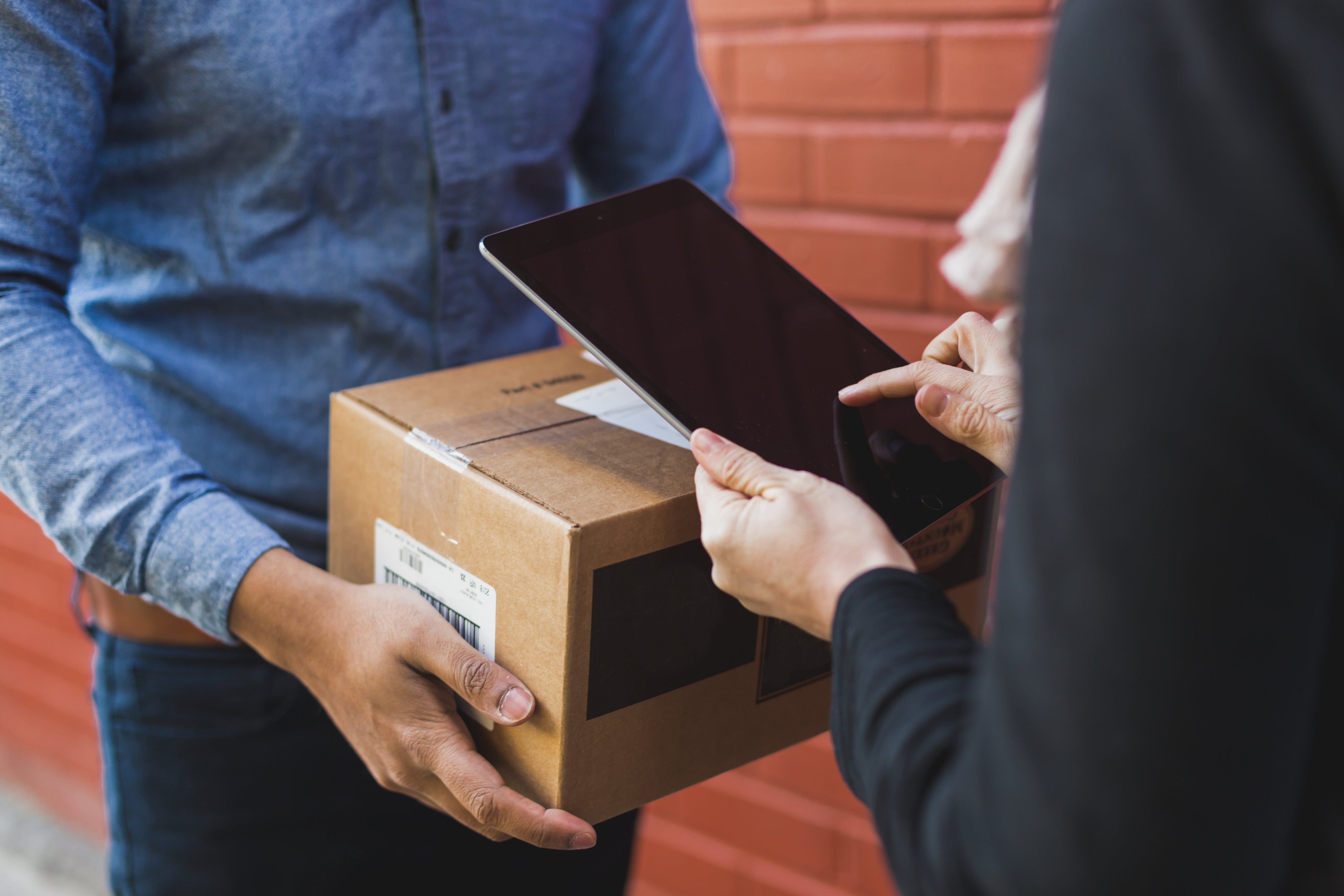 Person receiving cardboard shipping box while delivery person holds tablet for digital signature confirmation